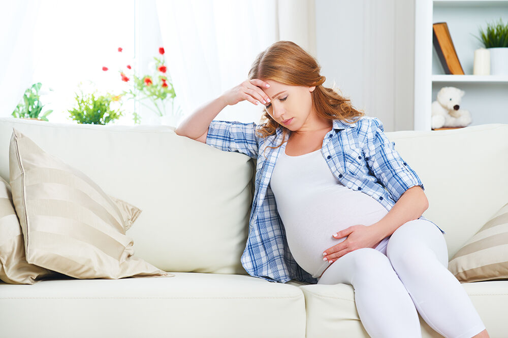 Gravid kvinne som sit i sofa og held seg til hovudet
