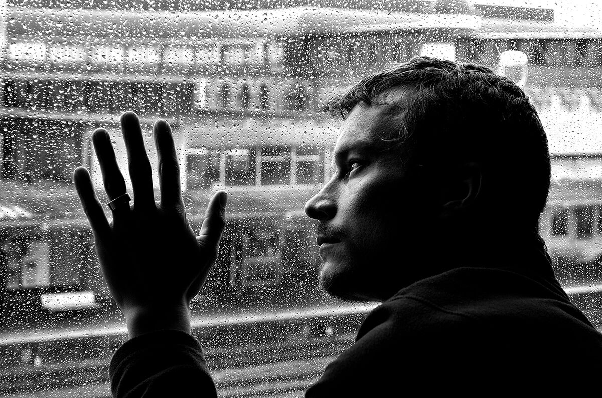 Mann med hovudet mot eit regnvått vindu