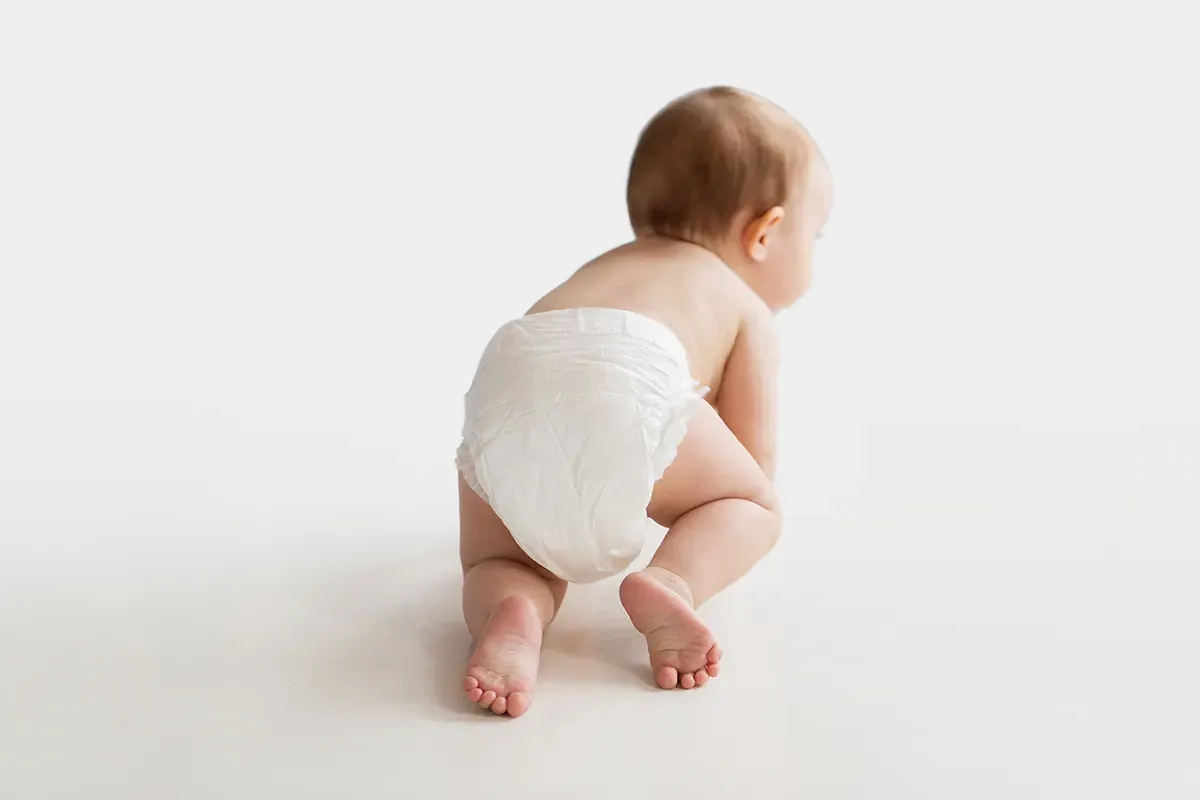 Ein baby med bleie som krabbar bortover golvet
