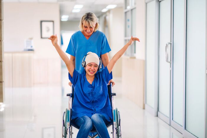 Kreftpasient i rullestol blir trillet av sykepleier.