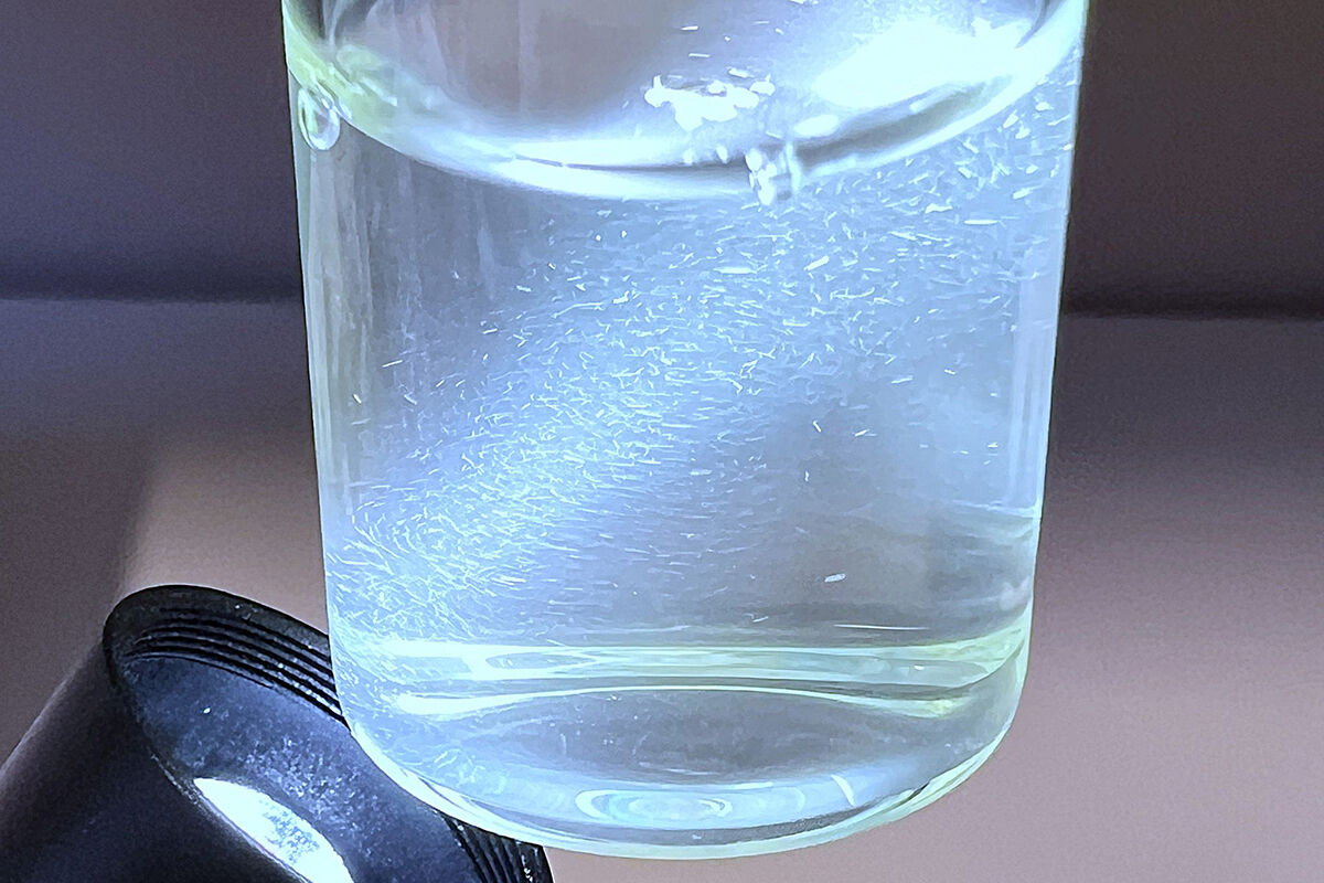 Ei lyskjelde lyser opp eit glas med klar væske. I væske er mange partiklar synlege