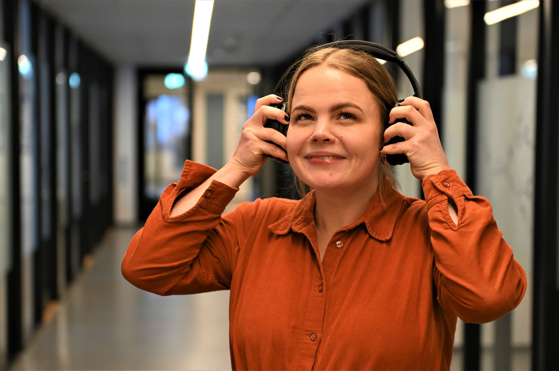 smilende kvinne i oransje skjorte som tar på hodetelefoner