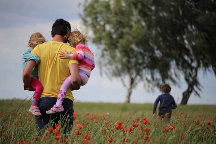 en mann bærer to barn i en blomstereng