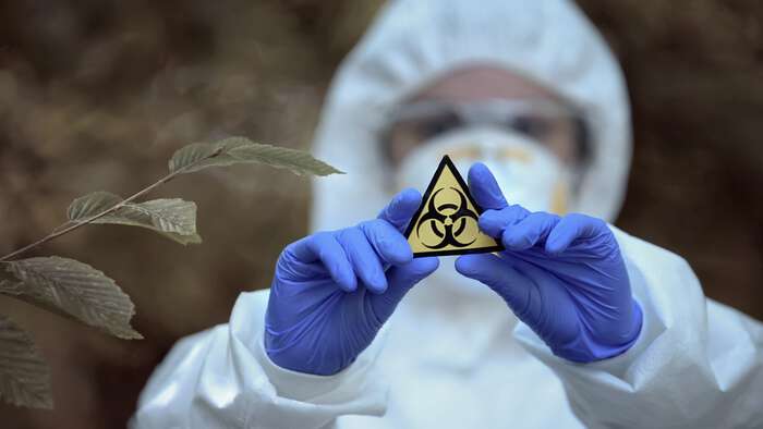 en person i fullt biologisk verneutstyr holder opp merket for biologisk farlig materiale