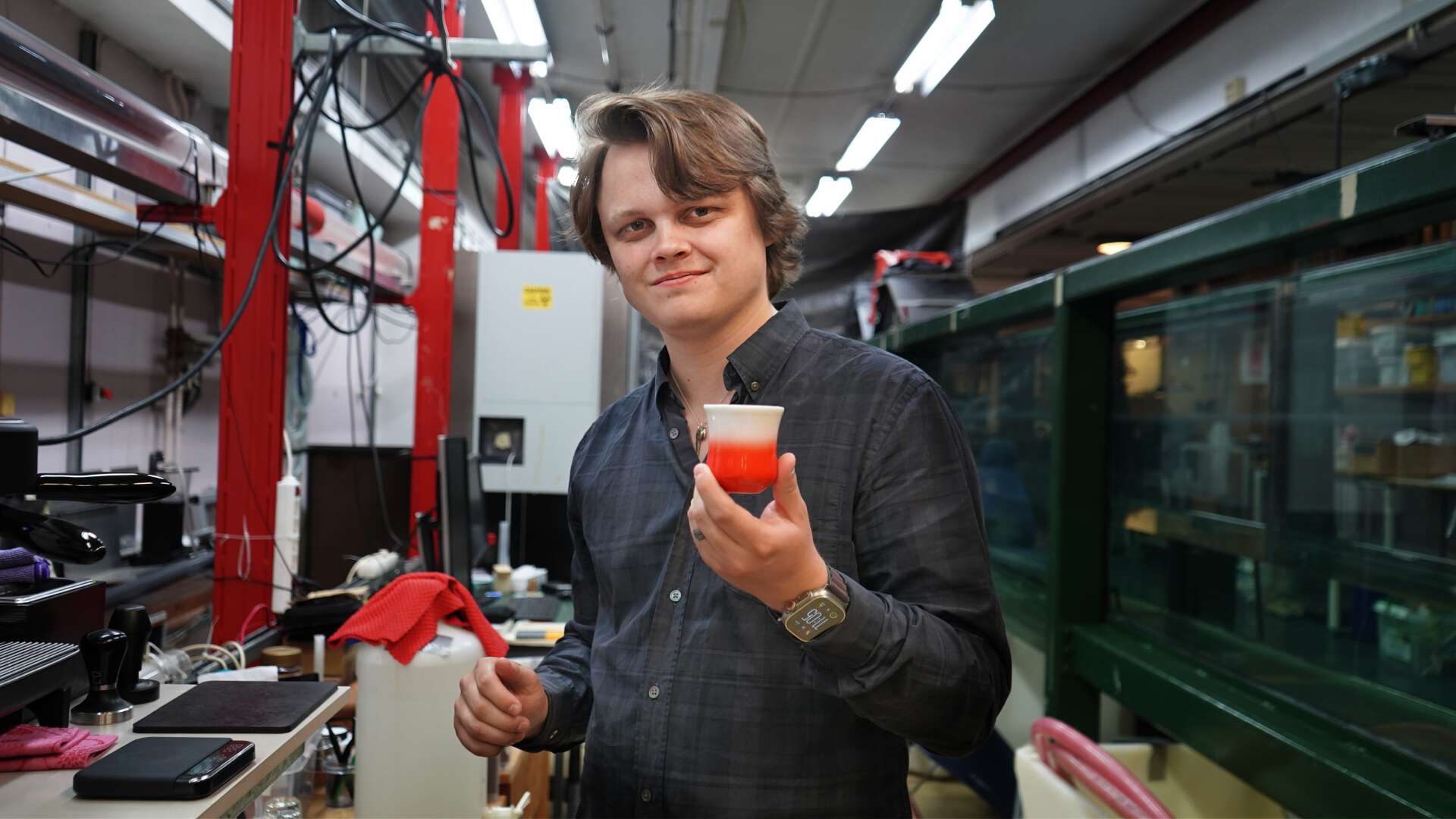 masterstudent holder fram en keramikkopp uten håndtak, med rød bunn.